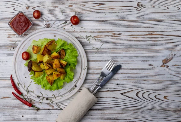 Hafif ahşap bir tahtanın üzerinde yeşil bir marul yaprağında baharatlı fırında patates.