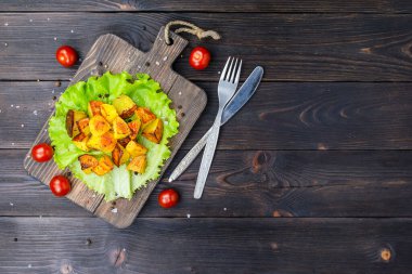 Koyu kahverengi ahşap bir tahtanın üzerinde yeşil bir marul yaprağı üzerinde çıtır çıtır patates.