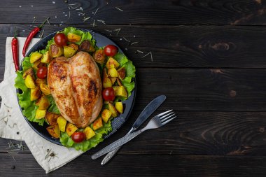 Fırın fırınında tavuk ve patates, yeşil marul yaprakları üzerinde, ahşap bir masada.