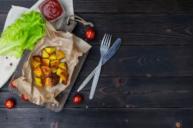 Fırında patates ve kiraz domatesleri kağıt üzerinde. Domates sosu, yeşil marul ve çatal bıçak takımı. Üst görünüm, metin için boşluk