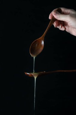 Bal, tahta bir kaşığa dökülür. Siyah arka plan. Şeffaf bal bir kaşıktan damlıyor. El, bal damlayan tahta bir kaşık tutar.