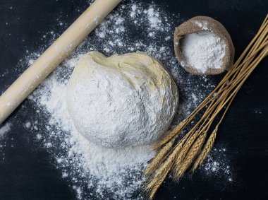 Üzerinde un serpiştirilmiş beyaz hamurlar karanlık bir masada yatıyor.