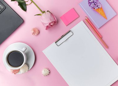 A black laptop, a lilac notebook, pink pencils on a light pink table