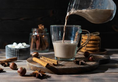 Hot cocoa pours from a transparent jug into a glass cup