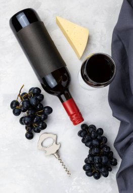 Arka planda bir şişe ve bir bardak kırmızı şarap. Masanın üzerinde siyah üzüm fırçaları. Arka planda bir tirbuşon ve bir parça peynir. Üst görünüm
