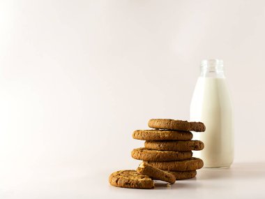 Açık bej arkaplanlı yulaf ezmeli kurabiyeler. Arka planda bir şişe süt. Mesaj için yer var. Hafif arkaplan