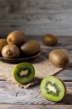 Olgun kivinin yarısı açık kahverengi bir ahşap masada yatar. Arka plandaki ahşap tabakta bütün kivi.