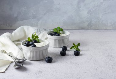 Masadaki beyaz vazolarda yaban mersinli yoğurt. Vazoların yanında yabanmersini ve nane yaprağı. Hafif arkaplan, metin için boşluk