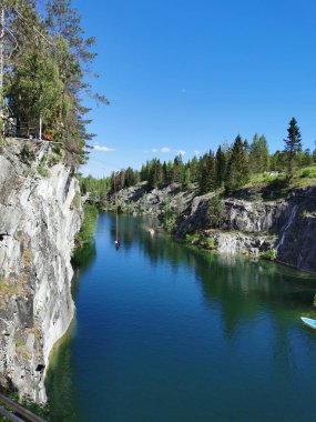 Ruskeala Dağ Parkı 'ndaki Mermer Kanyon' un turkuaz suyunun gözlem güvertesinden gökyüzünün yansıması ve güneşli bir yaz gününde ağaçların görüntüsü..