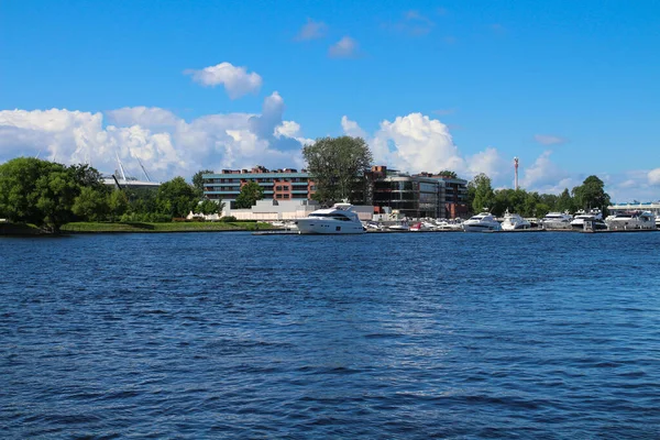 Nehirdeki yatların demirlemesi evlerin arka planına ve bulutlu mavi gökyüzüne karşı. St. Petersburg.