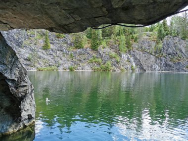 Güneşli bir yaz gününde Ruskeala Dağ Parkı 'nda ağaçların yetiştiği su basmış Mermer Kanyon' un yamacındaki mağaranın manzarası..