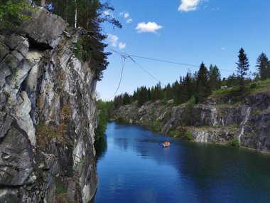 Güneşli bir yaz gününde Ruskeala Dağ Parkı 'ndaki Mermer Kanyon' un turkuaz sularında yüzen kayalıkların ve teknelerin görüntüsü.