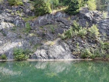 Güneşli bir yaz gününde Ruskeala dağ parkında ağaçların büyüdüğü su basmış Mermer Kanyon 'un yamacına bakın..