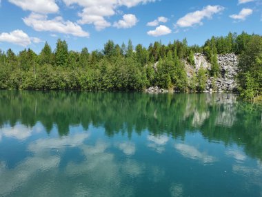 Göl kıyısında, Ruskeala dağ parkında, ağaçları ve gökyüzünü yansıtan turkuaz suyla aydınlık..