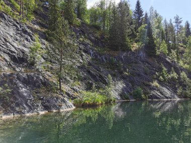 Güneşli bir yaz gününde Ruskeala dağ parkında ağaçların büyüdüğü su basmış Mermer Kanyon 'un yamacına bakın..