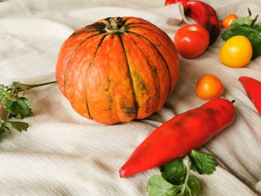 Yeşil çizgili turuncu balkabağı, turuncu, sarı ve kırmızı domatesler, kırmızı biber ve nane şekerleri açık bir kumaşın üzerinde bulunur. Yan görünüm.