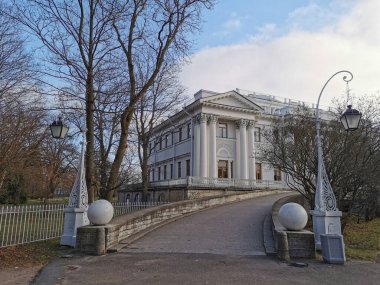 Saint-Petersburg 'da. - Rusya. Kaldırım taşlarından Elaginoostrovsky Sarayı 'na giriş, altında taş toplar ve yapraksız ağaçlar bulunan, St. P sonbahar parkında bulutlu mavi bir gökyüzüne bakan eski güzel fenerlerle çevrili.