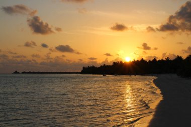 Maldivler 'de güzel bir gün batımı. Sun Island Oteli ve Spa. Beyaz kum, sakin okyanus, bulutlu turuncu gökyüzü.