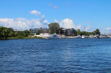 Nehir kıyısındaki yatların demirlemesi evlerin arka planına ve bulutlu mavi gökyüzüne karşı. St. Petersburg.