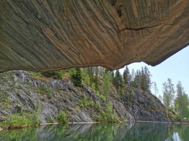 Güneşli bir yaz gününde Ruskeala Dağ Parkı 'ndaki su basmış Mermer Kanyon' un dik yamacında desenli tavanı olan mağaranın manzarası..