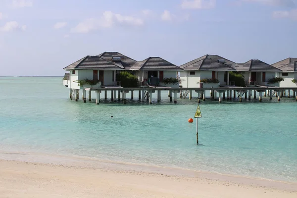 Maldivler 'de sabah, Hint Okyanusu kıyılarında beyaz kumlar, mercanlar ve villalar gök mavisi gökyüzüne karşı bulutlarla kaplı.