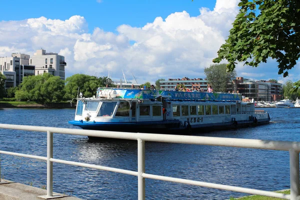 SAINT PETERSBURG . RUSSIA. A mooring excursion boat with tourists with an open upper deck against the backdrop of houses, a tower and a blue sky with clouds. St. Petersburg.