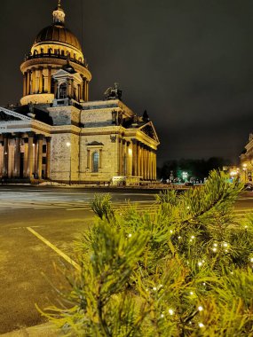 Pine branches decorated with garlands for Christmas and New Years, behind which is St. Isaac's Cathedral in St. Petersburg on an early winter morning.