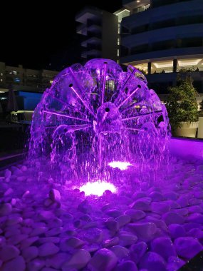 Protaras 'ta Kıbrıs' ta bir gece. Beyaz taşların üzerinde bir top şeklinde aydınlatılmış mor bir çeşme..