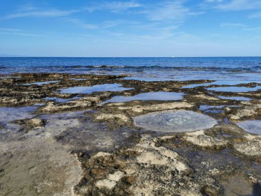 Protaras. Famagusta bölgesi. Kıbrıs. Uzun sert lavlar, Akdeniz kıyıları beyaz bir yatı ve güzel bulutları olan mavi bir gökyüzü olan denizin arka planına karşı..