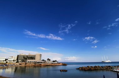 Protaras. Famagusta bölgesi. Kıbrıs. Akdeniz 'deki bir körfezde kumlu bir sahil manzarası. Dünyanın en büyük yelkenli yatı. Mavi gökyüzüne karşı sekiz güverteli bir motosailer..