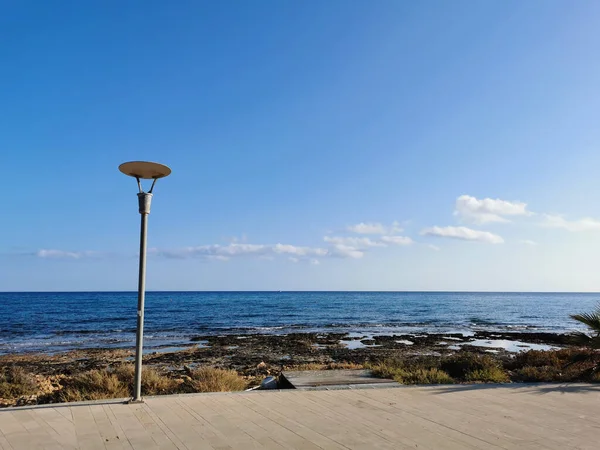 Protaras. Famagusta bölgesi. Kıbrıs. Akdeniz kıyısında bir fenerle bir gezinti, deniz manzarası, dalgalar ve bulutlu mavi gökyüzü..