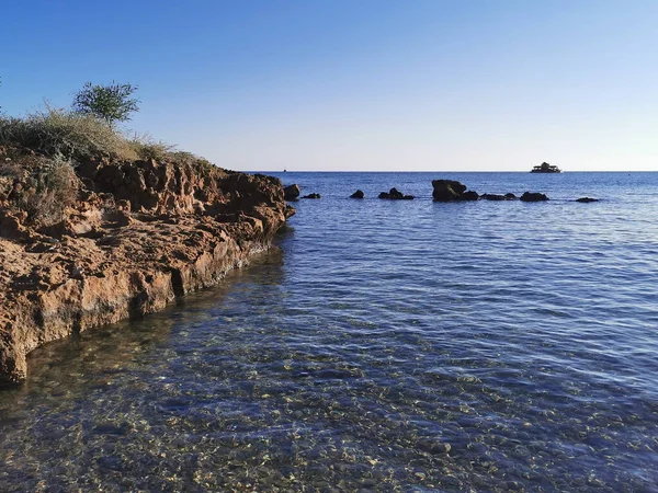 Protaras. Famagusta bölgesi. Kıbrıs. Akdeniz 'in sularında kıyıya yakın büyük taşlar mavi bulutsuz bir gökyüzü ve sarı bir turist teknesinin arka planına karşı..