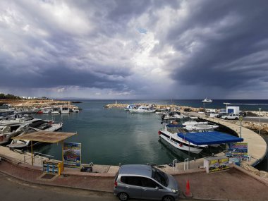 Protaras. Kıbrıs. Rıhtım, Akdeniz körfezinde küçük gemileri, yatları ve tekneleri olan liman dramatik bir gökyüzünün arka planına karşı..