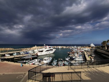 Protaras. Kıbrıs. Rıhtım, Akdeniz körfezinde küçük gemileri, yatları ve tekneleri olan liman dramatik bir gökyüzünün arka planına karşı..