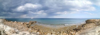 Protaras. Famagusta bölgesi. Kıbrıs. Panorama. Akdeniz 'in taş kıyıları, denizde beyaz bir gemi ve dramatik bir gökyüzüne karşı dünyanın en büyük yelkenli yatı..