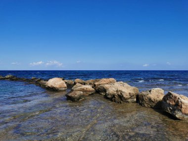 Protaras. Famagusta bölgesi. Kıbrıs. Akdeniz kıyıları, dalgalar, berrak su, bulutlu mavi gökyüzüne karşı taş bir sırt..