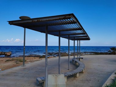 Protaras.Cyprus. Akdeniz 'in kayalık kıyısı uzun zamandır sertleşmiş lav, dalga ve bulutlu mavi gökyüzüne karşı temiz su. İki kişi balık tutuyor.