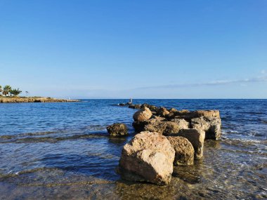 Protaras. Famagusta bölgesi. Kıbrıs. Akdeniz kıyıları, taştan bir tepe, sonunda bulutlu mavi gökyüzüne karşı bir balıkçı var..