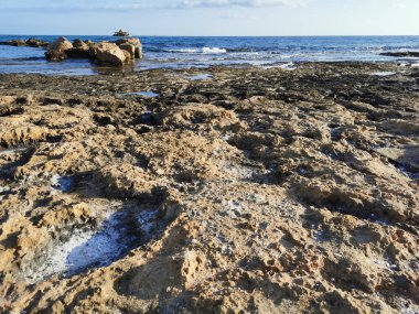 Protaras. Famagusta bölgesi. Kıbrıs. Akdeniz kıyıları, uzun sert lavlar, taş bir sırt, mavi gökyüzüne karşı denizde bir eğlence teknesi..