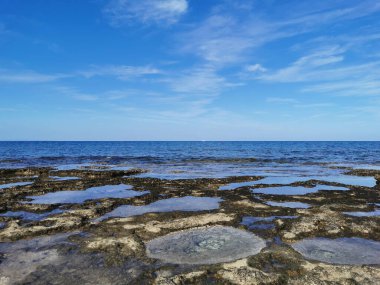 Protaras. Famagusta bölgesi. Kıbrıs. Uzun sert lavlar, Akdeniz kıyıları beyaz bir yatı ve güzel bulutları olan mavi bir gökyüzü olan denizin arka planına karşı..