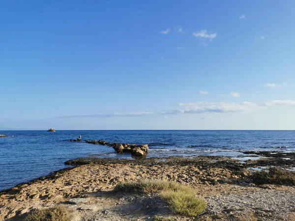 Protaras 法马古斯塔地区塞浦路斯 地中海的岩石海岸 一个石脊 尽头是一个渔夫 在大海中与蓝蓝的天空相映成趣的小船 — 图库照片