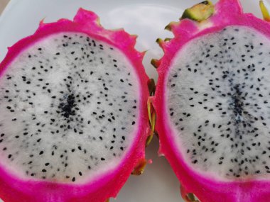 Pembe dışarıda ve beyaz pitahaya (pitahaya veya ejderha gözü) - Hylocereus kaktüsünün meyvesidir, ikiye bölünmüş, beyaz bir tabakta yatar..