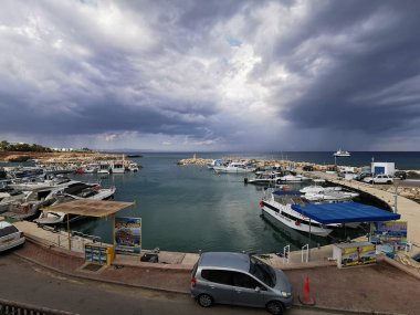 Protaras. Kıbrıs. 10.18.2021. Rıhtım, Akdeniz körfezinde küçük gemileri, yatları ve tekneleri olan liman dramatik bir gökyüzünün arka planına karşı..