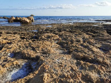 Protaras. Famagusta bölgesi. Kıbrıs. Akdeniz kıyıları, uzun sert lavlar, taş bir sırt, mavi gökyüzüne karşı denizde bir eğlence teknesi..