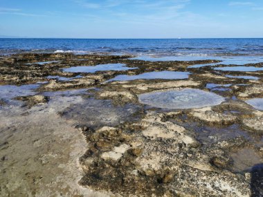 Protaras. Famagusta bölgesi. Kıbrıs. Uzun sert lavlar, Akdeniz kıyıları beyaz bir yatı ve güzel bulutları olan mavi bir gökyüzü olan denizin arka planına karşı..