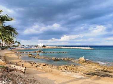 Protaras. Kıbrıs. Rıhtım, Akdeniz körfezinde küçük gemileri, yatları ve tekneleri olan liman dramatik bir gökyüzünün arka planına karşı..