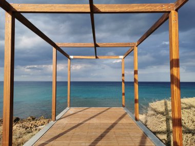 Akdeniz 'in turkuaz sularının üzerinde çarpıcı bir gökyüzüne karşı ahşap çerçeveli bir gözlem güvertesi..