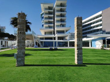 Protaras. Famagusta bölgesi. Kıbrıs. Otelin boş bölgesi, Akdeniz kıyılarında, mavi bulutsuz gökyüzüne karşı suni çimlerle kaplı..