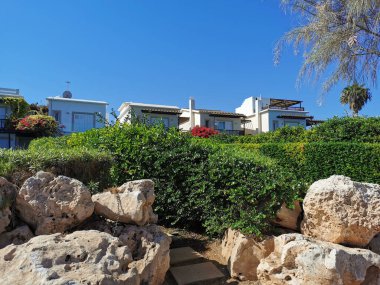 Protaras. Famagusta bölgesi. Kıbrıs. Akdeniz kıyılarında bulutsuz mavi gökyüzüne karşı duran bir villanın önündeki büyük taşlar ve güzel budanmış çalılar..