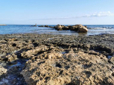 Protaras. Famagusta bölgesi. Kıbrıs. Akdeniz kıyıları, taştan bir tepe, sonunda bulutlu mavi gökyüzüne karşı bir balıkçı var..